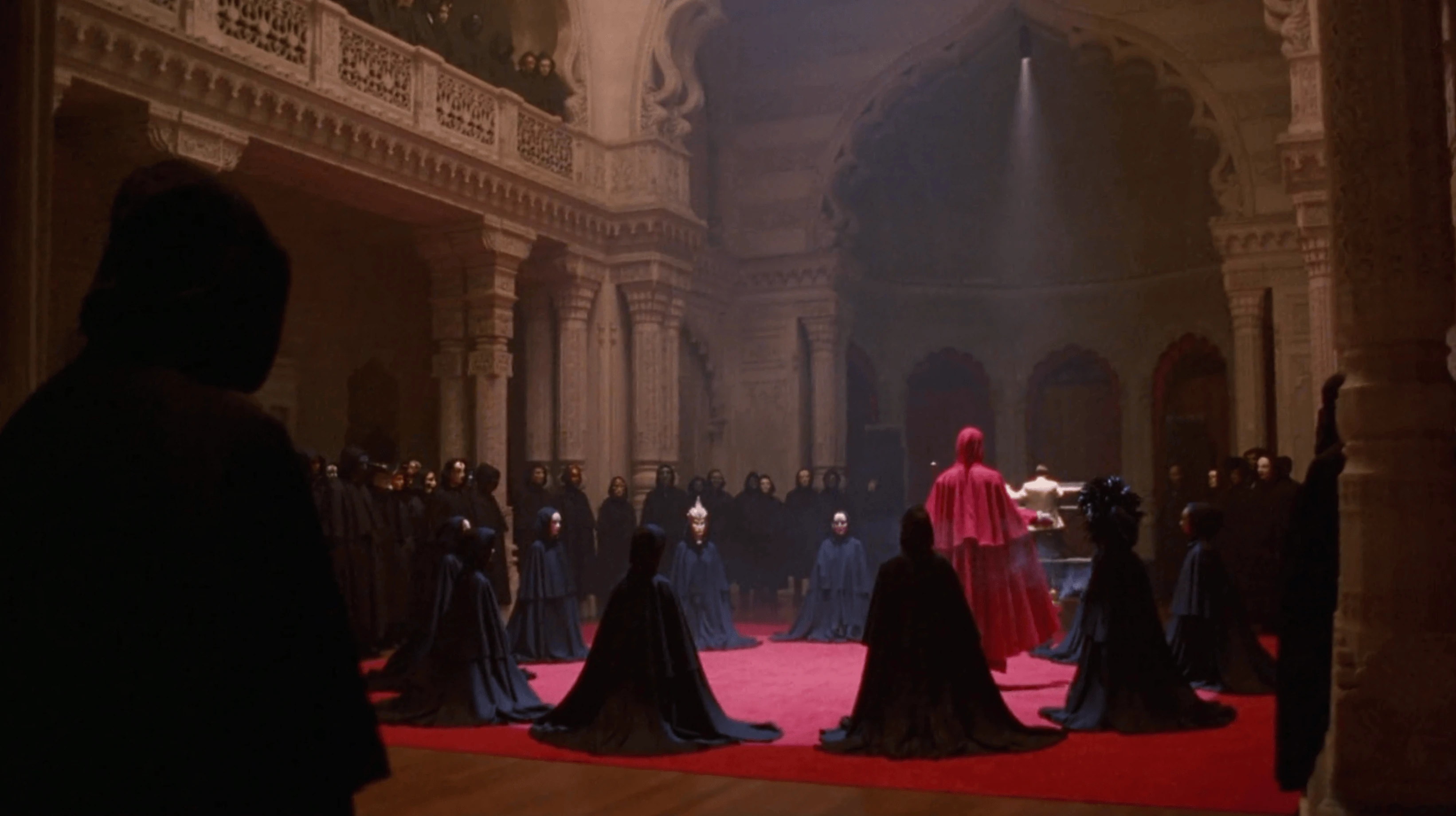 La cérémonie, vue large, figures encapuchonnées et officiant en rouge