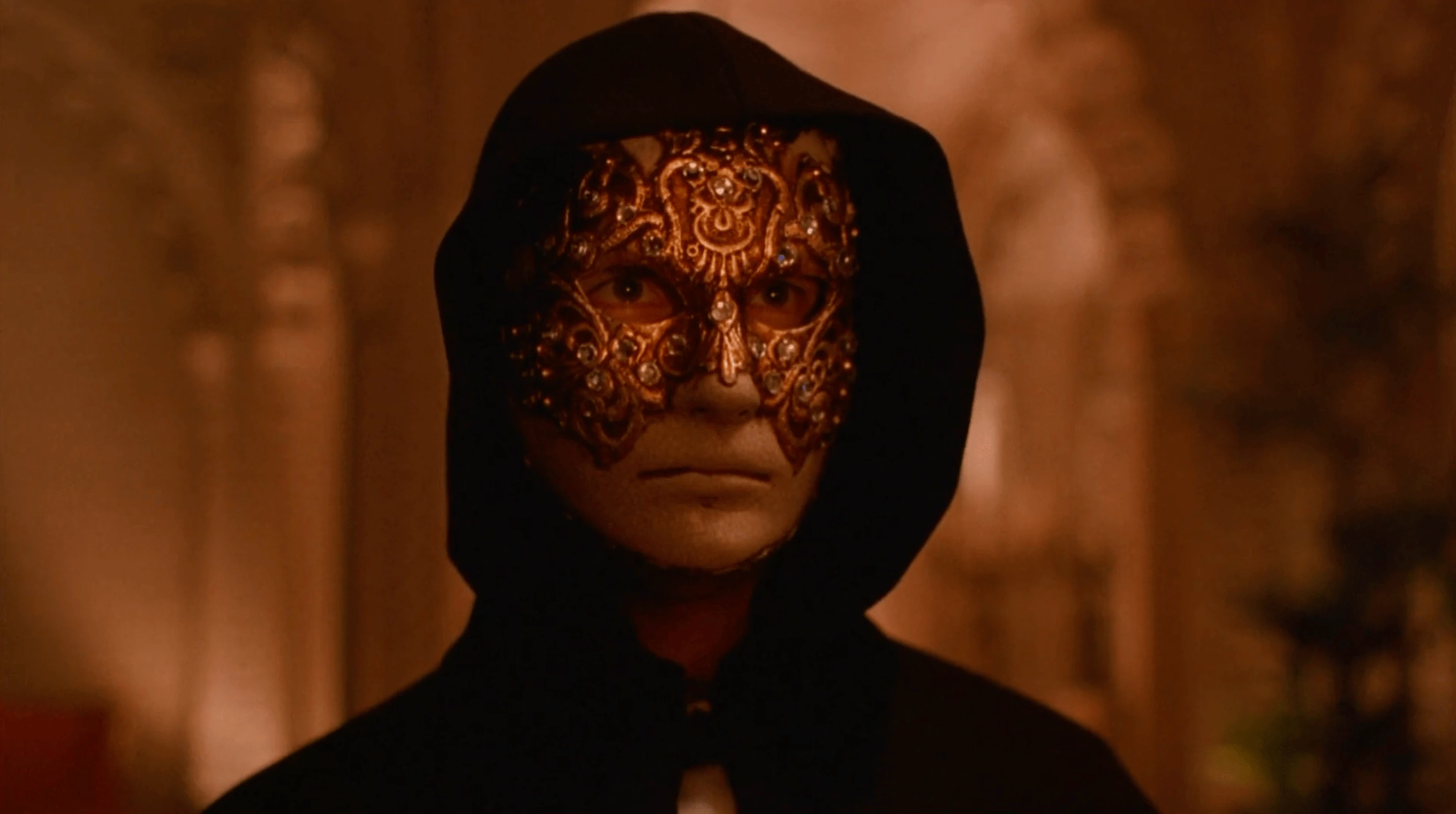 Masque doré orné, capuche noire, regard inconnu